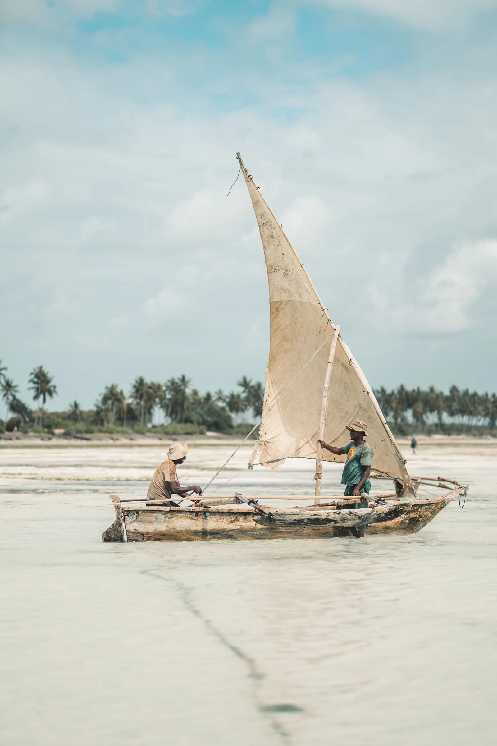 Two fishermen aboard a traditional wooden sailing boat in shallow water
